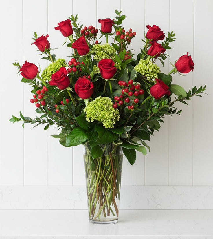 A vase of red roses with green hydrangeas and red berries.
