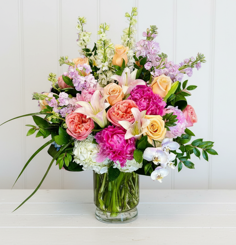 A clear glass vase filled with a vibrant arrangement of pink, peach, and white flowers.