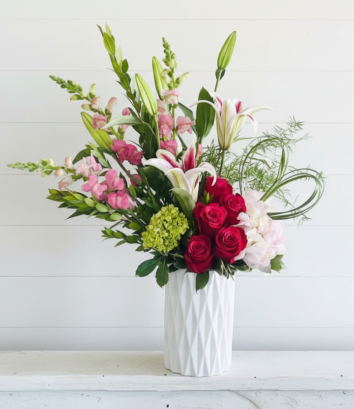A tall vase of pink snapdragons, red roses, and white lilies.
