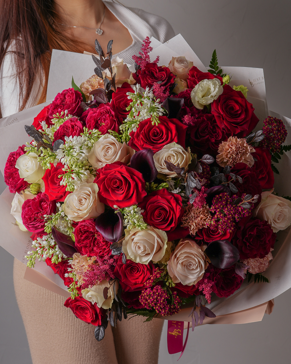 Bouquet of red, white, and pink roses with greenery held by a person.
