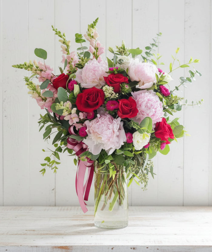 A bouquet of pink peonies and red roses in a glass vase.