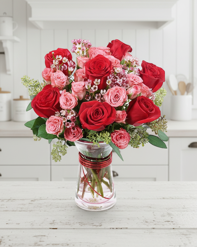 A bouquet of red roses and pink fillers in a glass vase.