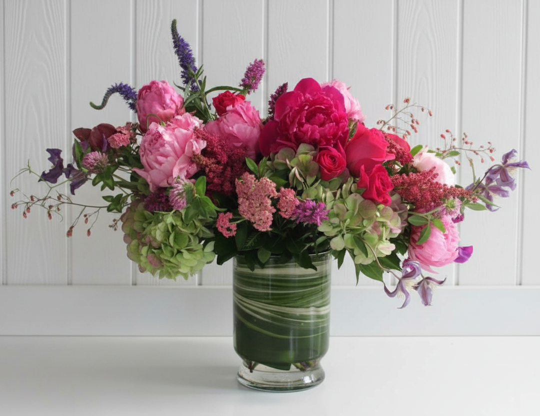 Bouquet of pink and red flowers in a glass vase on a white surface with a white paneled background