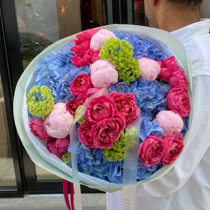 Person holding a large round bouquet of flowers with pink and blue colors.