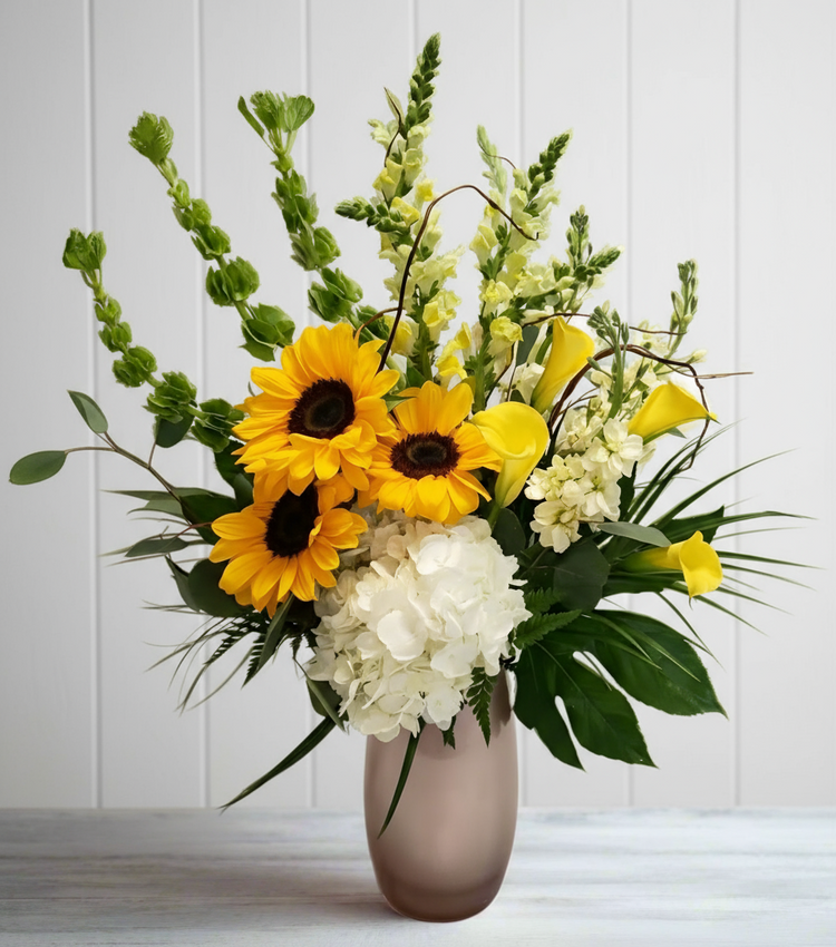 A vibrant arrangement of sunflowers, yellow calla lilies, and white hydrangeas in a vase.