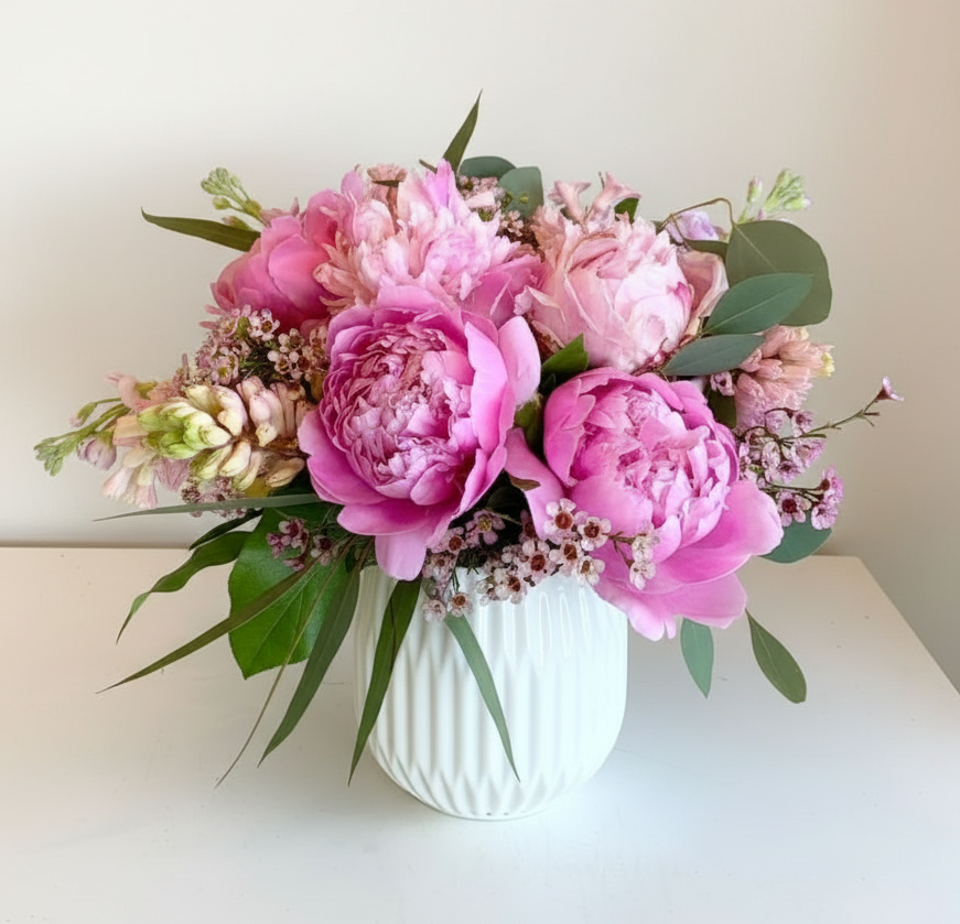 Bouquet of pink peonies and other flowers in a white vase on a light surface with a neutral background