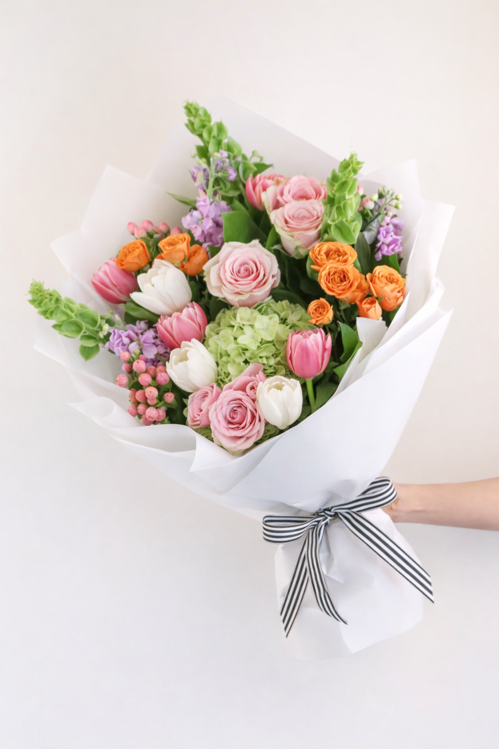 Bouquet of colorful flowers wrapped in white paper with a black and white striped ribbon on a light background.